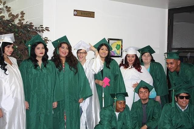 Group of Class of 2015 graduates in green and white caps and gowns posing indoors