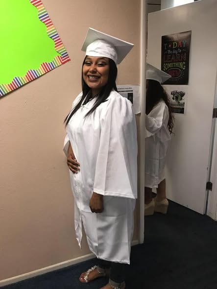 Class of 2017 graduate in white cap and gown smiling at Operation New Hope