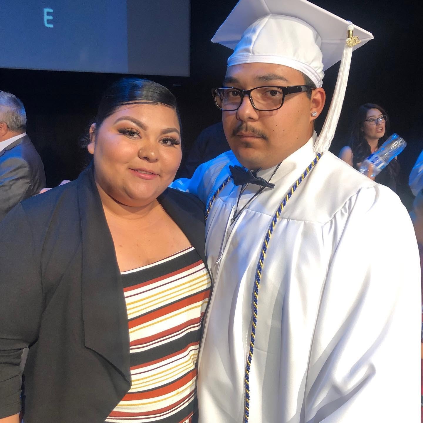Class of 2019 graduate in white cap and gown with supporter at graduation ceremony