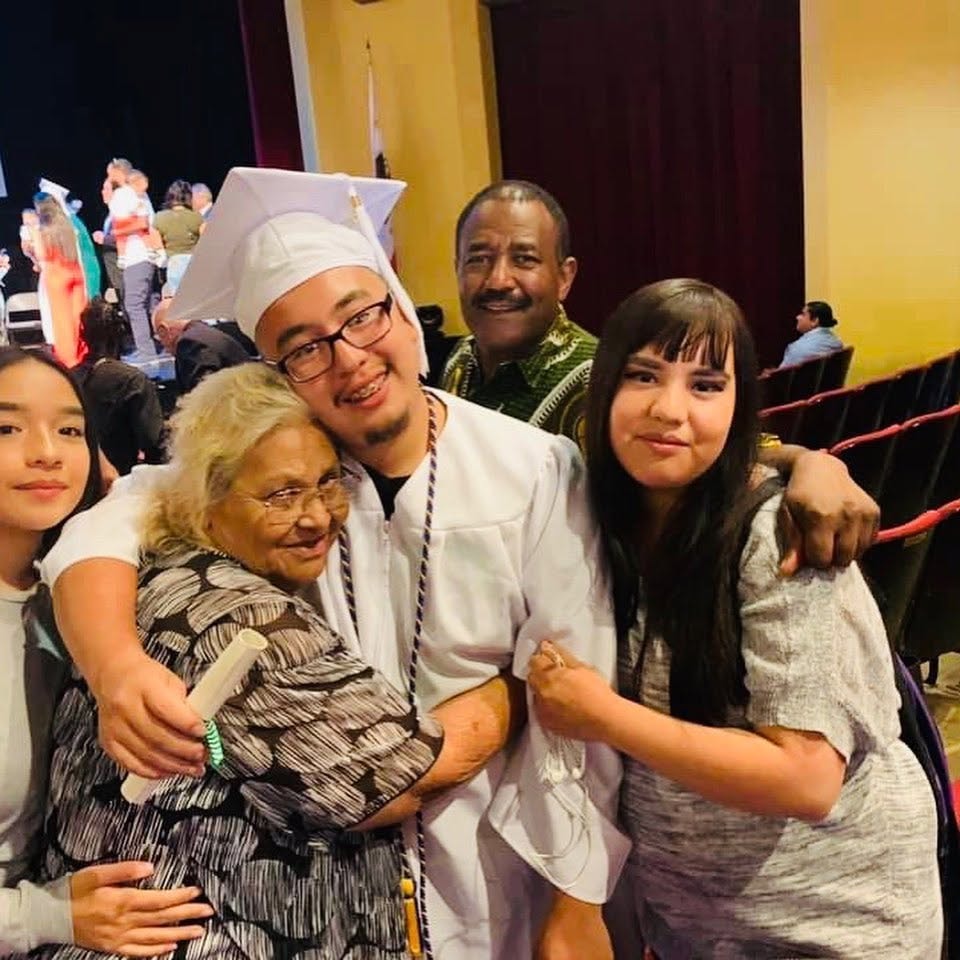 Class of 2019 graduate in white cap and gown embracing family members in theater after ceremony