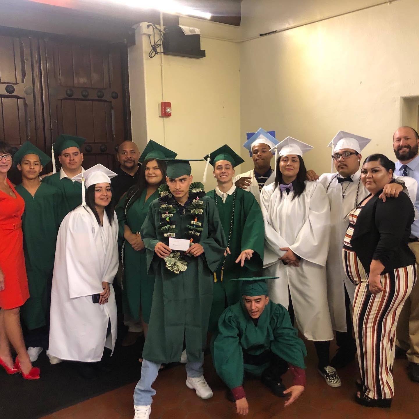 Group of Class of 2019 graduates in green and white gowns with staff at Operation New Hope
