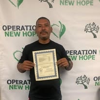 Graduate holding Security Guard Card certificate in front of Operation New Hope backdrop