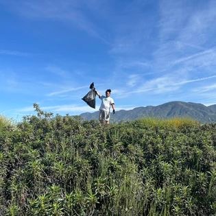 Student holding trash bag on hillside during community cleanup