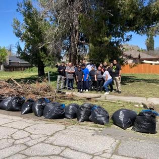 Group of students and staff posing behind filled trash bags after neighborhood cleanup