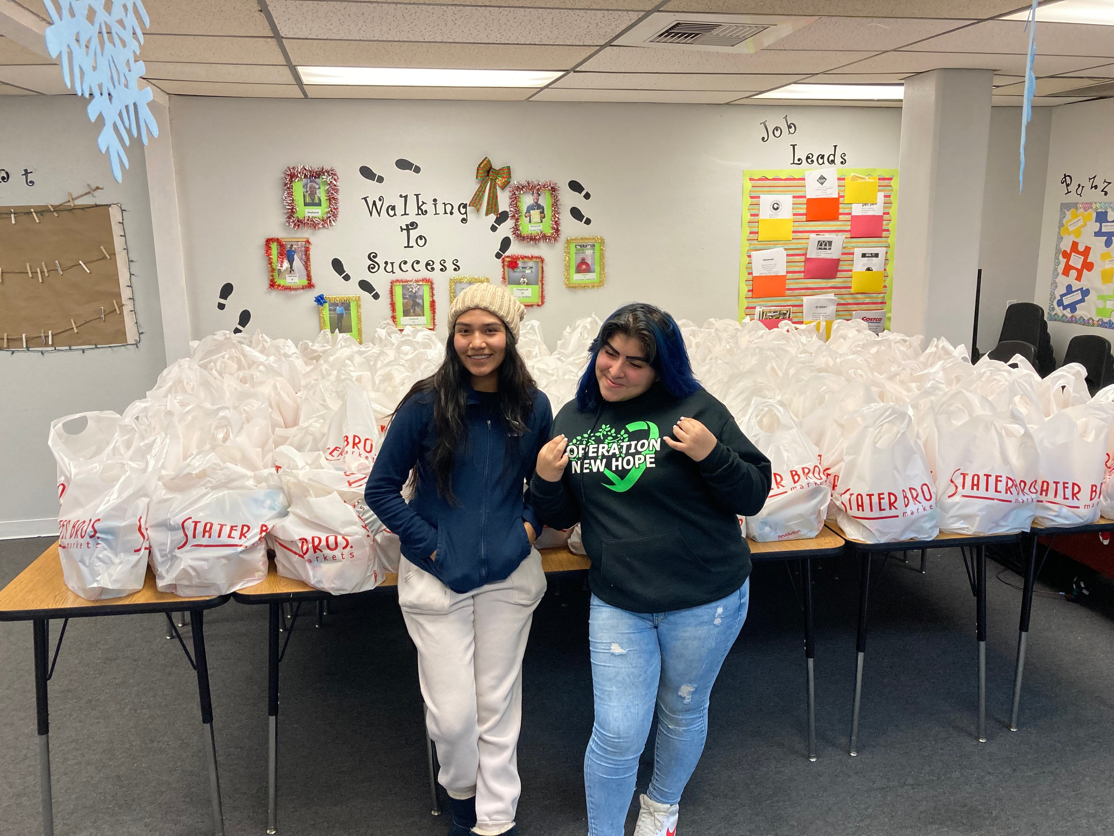 Two students standing in front of Stater Bros food bags at ONH Learning Center holiday food outreach