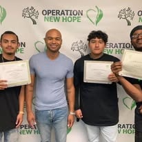 Four people holding certificates in front of Operation New Hope backdrop